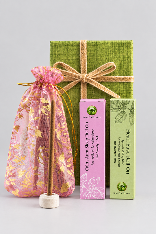 A gift set of herbal wellness products including a pink drawstring pouch with a wooden incense stick, a pink box of Calm Aura Roll On, and a green box of Head Ease Roll On for head ache arranged on a marble surface with flowers and a candle in the background.